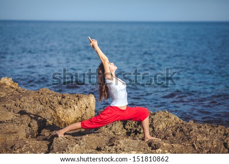 An attractive young woman doing a yoga pose for balance and stretching near the sea