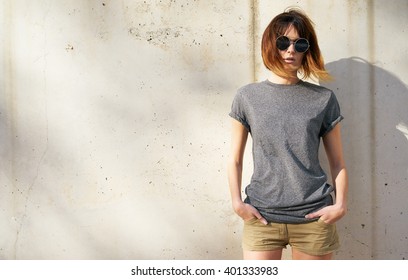 attractive young woman dressed in a gray blank t-shirt posing on a background of a concrete wall in the rays of the setting sun
