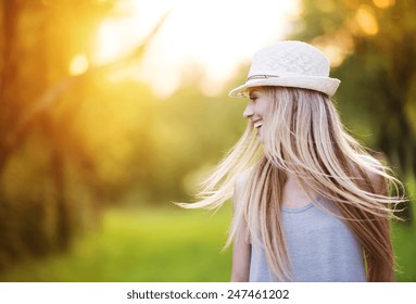 Attractive Young Woman Enjoying Her Time Outside In Park With Sunset In Background.