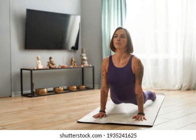 Attractive young woman exercising, doing Upward Facing Dog yoga pose on a mat in living room at home. Fitness, relaxation, stay home concept
