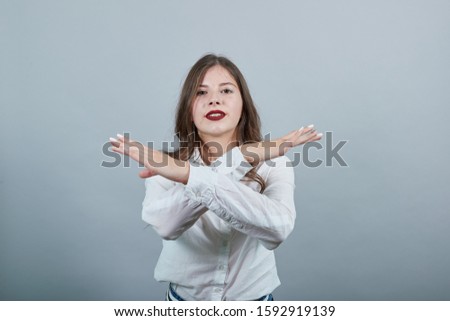 Attractive young woman in fashion white shirt doing stop, NO gesture, looking serious at camera isolated on gray background in studio. People sincere emotions, lifestyle concept.