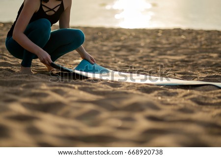 Attractive young woman folding green yoga or fitness mat after working out at the beach.