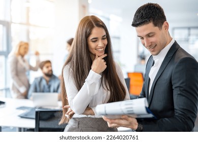 Attractive young woman in formal wear checking financial reports and paperwork with handsome good looking man in suit while standing in office. - Powered by Shutterstock