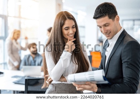Attractive young woman in formal wear checking financial reports and paperwork with handsome good looking man in suit while standing in office.