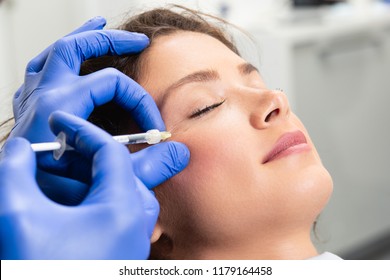 Attractive young woman is getting a rejuvenating facial injections. She is sitting calmly at clinic. The expert beautician is filling female wrinkles by hyaluronic acid. - Shutterstock ID 1179164458