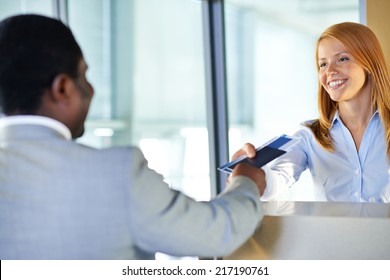 Attractive Young Woman Giving Passport And Ticket Back To Businessman At Airport Check-in Counter