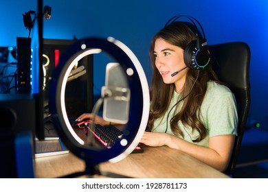 Attractive Young Woman With Headphones Speaking To An Online Player With A Microphone While Playing And Live Streaming Her Video Game In In A Gaming Computer 