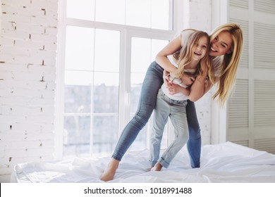 Attractive young woman and her little cute daughter are having fun in bed while being at home together. Happy Mother's Day!