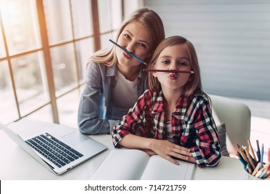 Attractive Young Woman And Her Little Cute Daughter Are Sitting At The Table And Having Fun While Doing Homework Together. Mother Helps Daughter With Her School Classes.