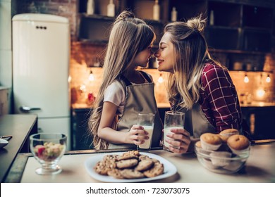 Attractive young woman with her little cute daughter are cooking on kitchen. Drinking milk, eating cakes and cookies.