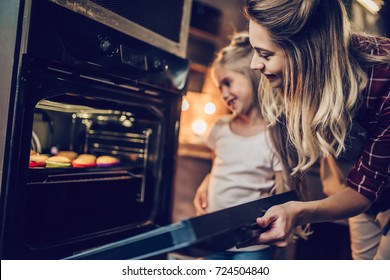 Attractive young woman with her little cute daughter are cooking cakes on kitchen.