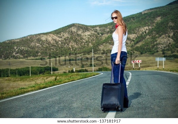 Attractive young\
woman hitchhiking along a\
road.