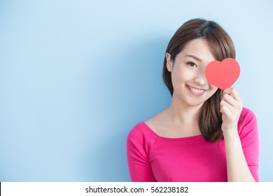 Attractive young woman holding red love hearts over eyes isolated on blue background