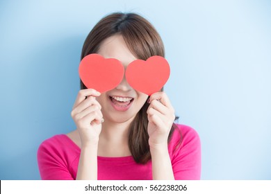 Attractive young woman holding red love hearts over eyes isolated on blue background