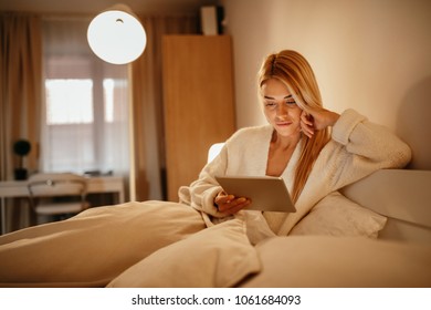 Attractive young woman holding a tablet in the bedroom