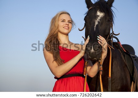 Attractive young woman hugging a horse. Portrait on blue sky background. Beautiful blonde smiling looking away. Bottom-up view