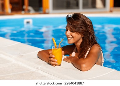 Attractive young woman leaning on the edge of a swimming pool, relaxing while on summer vacation, sunbathing and drinking cocktails - Powered by Shutterstock