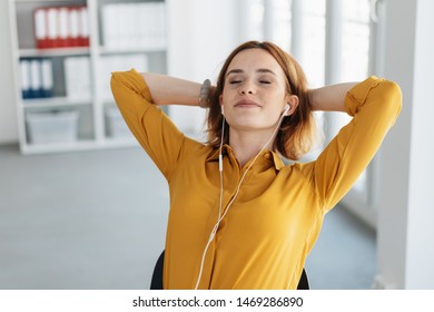 Attractive young woman listening to her music during a break at the office leaning back in her chair with eyes closed and a happy smile