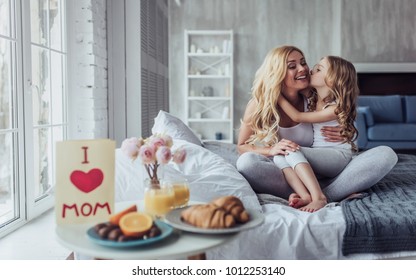 Atractiva mujer joven con una niña linda está pasando tiempo juntos en casa sentada en la cama. Feliz concepto familiar. Desayuno en la cama el día de la madre. Foto de stock