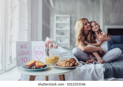 Attractive young woman with little cute girl are spending time together at home while sitting on bed. Happy family concept. Breakfast in bed on Mother's day. - Powered by Shutterstock