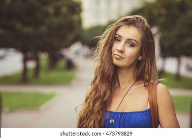 Attractive young woman with long curly hair poses in blue summer dress