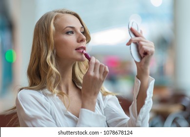 Attractive Young Woman Looking Into A Compact Mirror And Putting On Make-up