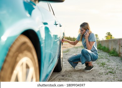 Attractive Young Woman Looking Sad, Calling Car Service, Assistance Or Tow Truck While Having Troubles With Her Auto, Checking Wheel After Car Breakdown On Local Road Side, Horizontal Shot