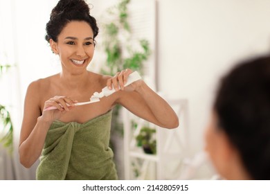 Attractive Young Woman With Lovely Smile Wearing Towel After Shower, Applying Toothpaste On Brush Near Mirror At Home, Blank Space. Dental Care, Daily Hygiene Concept