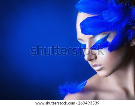 Attractive young woman with make-up with bright blue feathers on a blue background