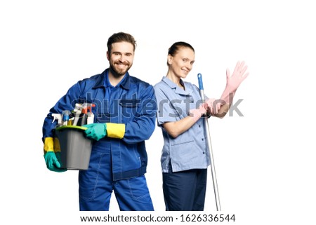 Attractive young woman and man  in cleaning uniform and rubber gloves holding Basket with means for wet cleaning woman puts on a rubber glove and smiles, isolated on white background.