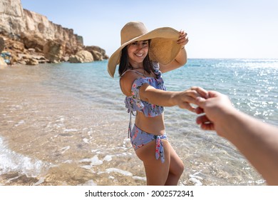 An Attractive Young Woman On The Seashore In A Swimsuit And A Big Hat Walks By The Hand With A Guy.