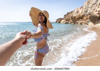 An Attractive Young Woman On The Seashore In A Swimsuit And A Big Hat Walks By The Hand With A Guy.