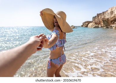 An Attractive Young Woman On The Seashore In A Swimsuit And A Big Hat Walks By The Hand With A Guy.