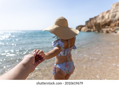 An Attractive Young Woman On The Seashore In A Swimsuit And A Big Hat Walks By The Hand With A Guy.