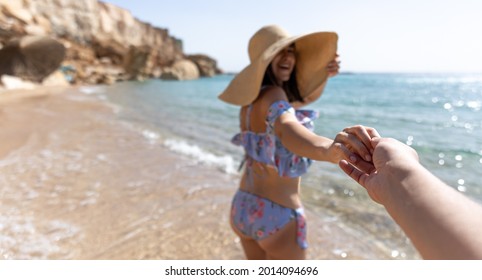 An Attractive Young Woman On The Seashore In A Swimsuit And A Big Hat Walks By The Hand With A Guy.