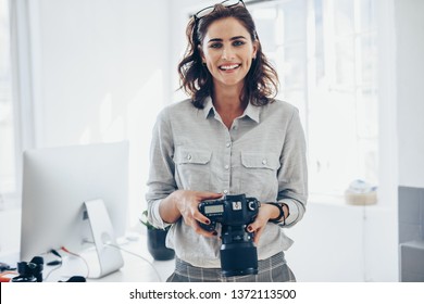 Attractive young woman photographer with her professional camera. Woman photographer with digital camera in office.