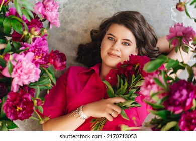 An Attractive Young Woman In A Pink Blouse With Peony Flowers On The Floor. Flower Shop. Training As A Florist. Perfumes For The Body And Home. The Beauty Of Flowers.