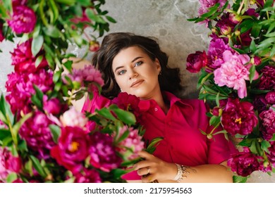 An Attractive Young Woman In A Pink Blouse With Peony Flowers On The Floor. Flower Shop. Training As A Florist. Perfumes For The Body And Home. The Beauty Of Flowers.