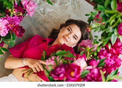 An Attractive Young Woman In A Pink Blouse With Peony Flowers On The Floor. Flower Shop. Training As A Florist. Perfumes For The Body And Home. The Beauty Of Flowers.