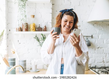 Attractive Young Woman Plus Size Body Positive In Blue Jeans And White Shirt Using Cellphone At Home Kitchen