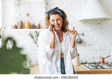 Attractive Young Woman Plus Size Body Positive In Blue Jeans And White Shirt Talking On Cellphone At Home Kitchen