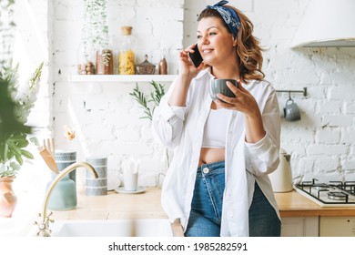 Attractive Young Woman Plus Size Body Positive In Blue Jeans And White Shirt Talking On Cellphone At Home Kitchen