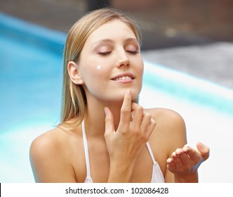 Attractive young woman in pool putting sunscreen on her face