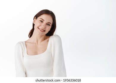 Attractive Young Woman Posing Cute On White Studio Backround, Tilt Head And Smile At Camera Softly, Making Gentle Face Expression, Standing Over White Background