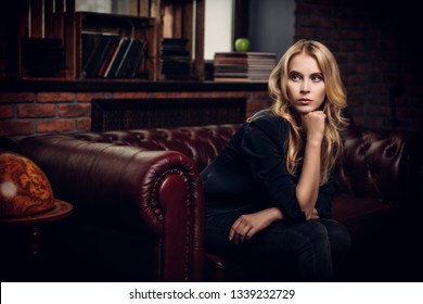 Attractive young woman posing on a leather sofa in a room with brick walls. Loft style interior. Beauty, fashion. Evening makeup and hairstyle.