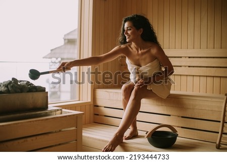 Attractive young woman pouring water onto hot stone in the sauna