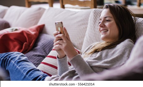 Attractive young woman relaxing at home on her couch using her cell phone