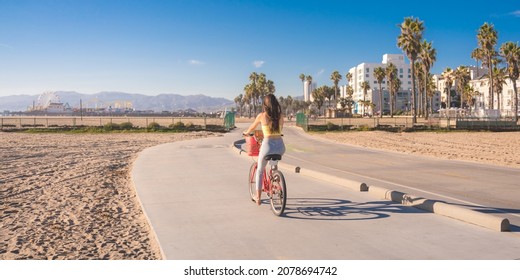 Attractive young woman riding bike near beach with palm trees, Santa Monica, Los Angeles, California