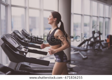 Attractive young woman runs on a treadmill is engaged in fitness sport club