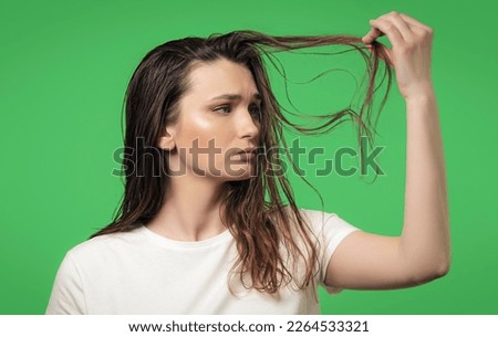 Attractive young woman is sad about her dirty, oily and greasy hair, isolated on a green background. Need a shampoo concept. Easily removable and replaceable chroma key background.